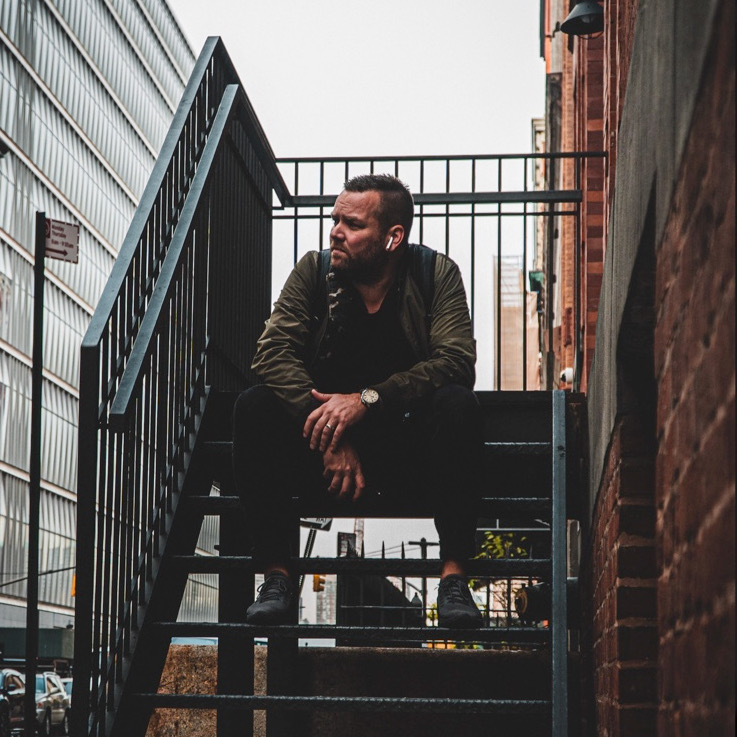 A man sitting on top of stairs next to metal railing.